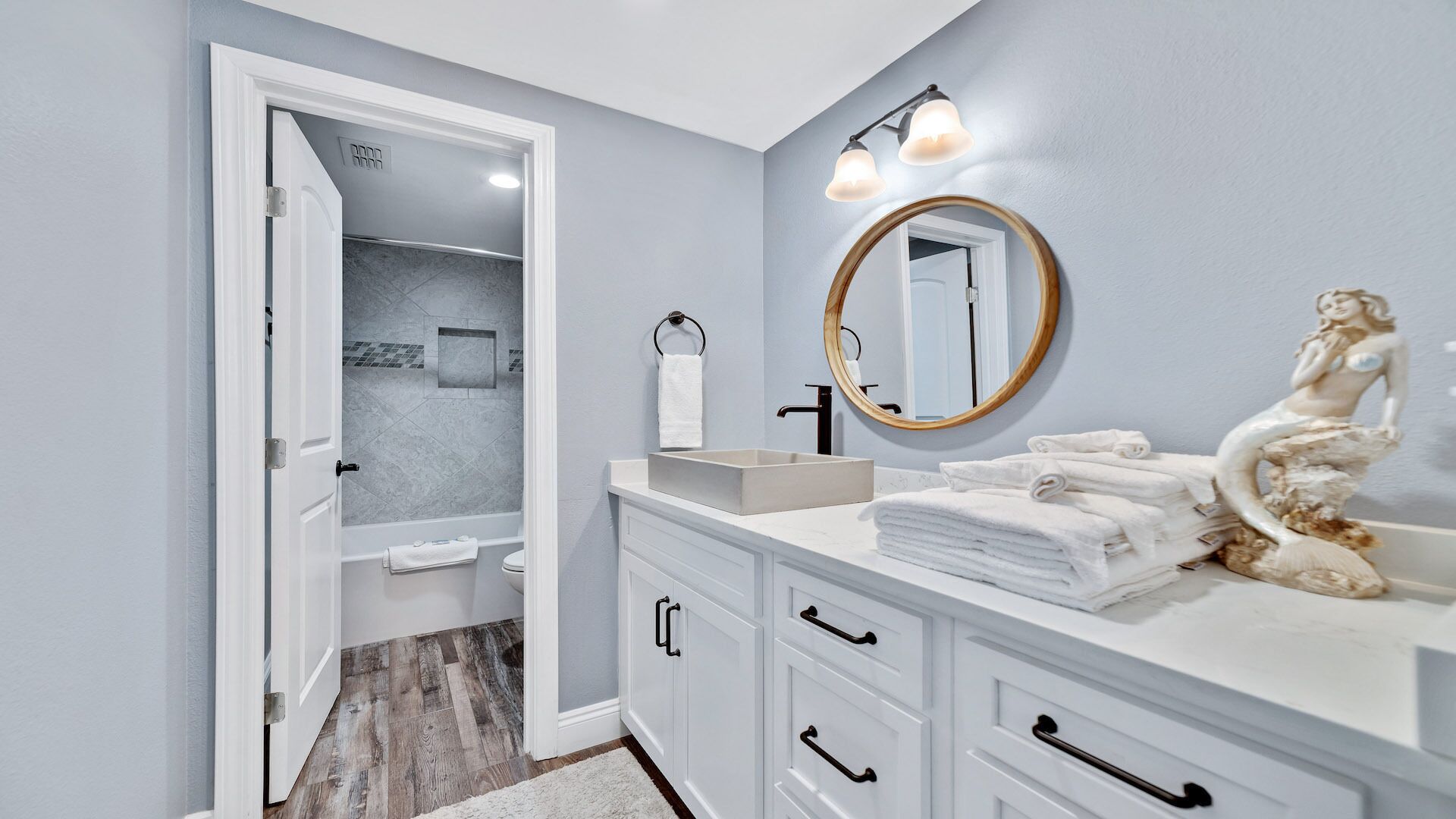 A modern bathroom with a walk-in shower, a vanity with a large mirror, and a statue on the counter.