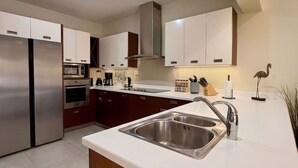Une cuisine moderne dotée d’appareils électroménagers en acier inoxydable, d’un îlot central avec un évier et de meubles de rangement en bois.