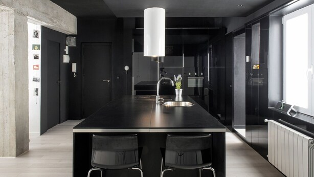 Et moderne køkken med en central ø, to barstole, en hængende lampe og udsigt til det tilstødende opholdsstue.