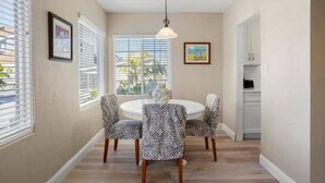 A dining area with a round table, patterned chairs, a hanging light fixture, and a view through the window.