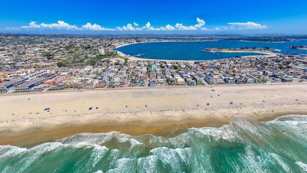 An aerial view of a coastal city with a beach, buildings, and a large body of water.