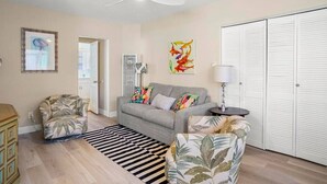 A living room with a sofa, two armchairs, a ceiling fan, a rug, a painting, and a white closet.