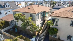 A residential building with a staircase leading to a second floor, surrounded by other houses and palm trees.