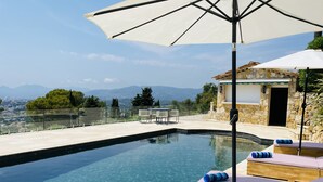 A pool area with clear blue water, wooden lounge chairs, and an umbrella. - Gorgeous 4 bedroom, 3 bathroom villa with private pool & sea view in Mougins (Mougins)