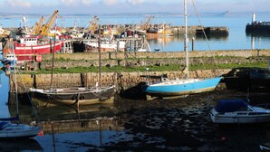 A harbor with various boats docked, including a red and white ship, a blue sailboat, and a white boat with a blue cover. - Belmont (Penzance)