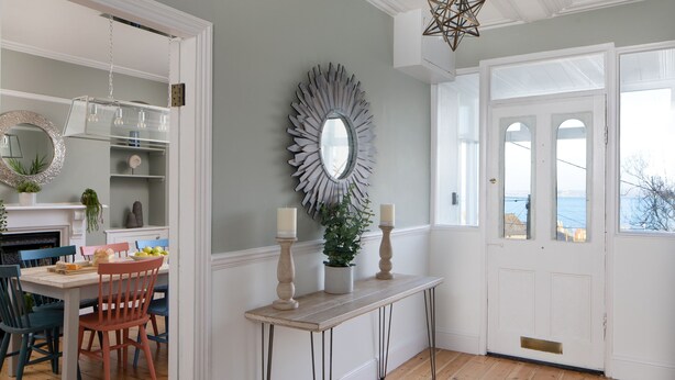 A dining area with a table set for four, a mirror, and a view of the sea through a door. - Belmont (Penzance)