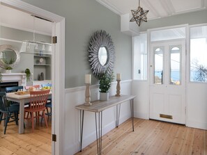 A dining area with a table set for four, a mirror, and a view of the sea through a door. - Belmont (Penzance)