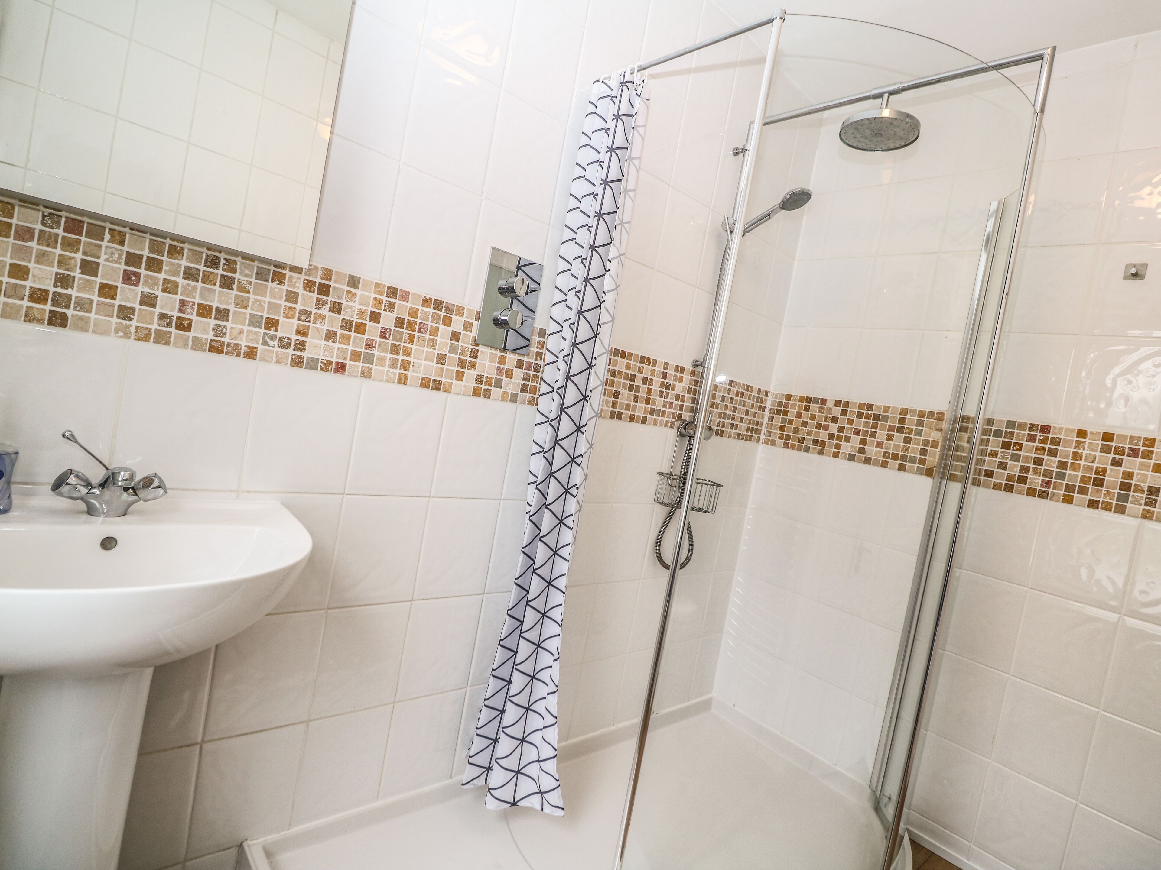 A bathroom with a glass shower enclosure, a sink with a modern faucet, and a tiled backsplash with a mosaic pattern.