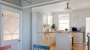 A kitchen with white cabinets, a wooden island, and a dining area with a table and chairs. - Belmont (Penzance)