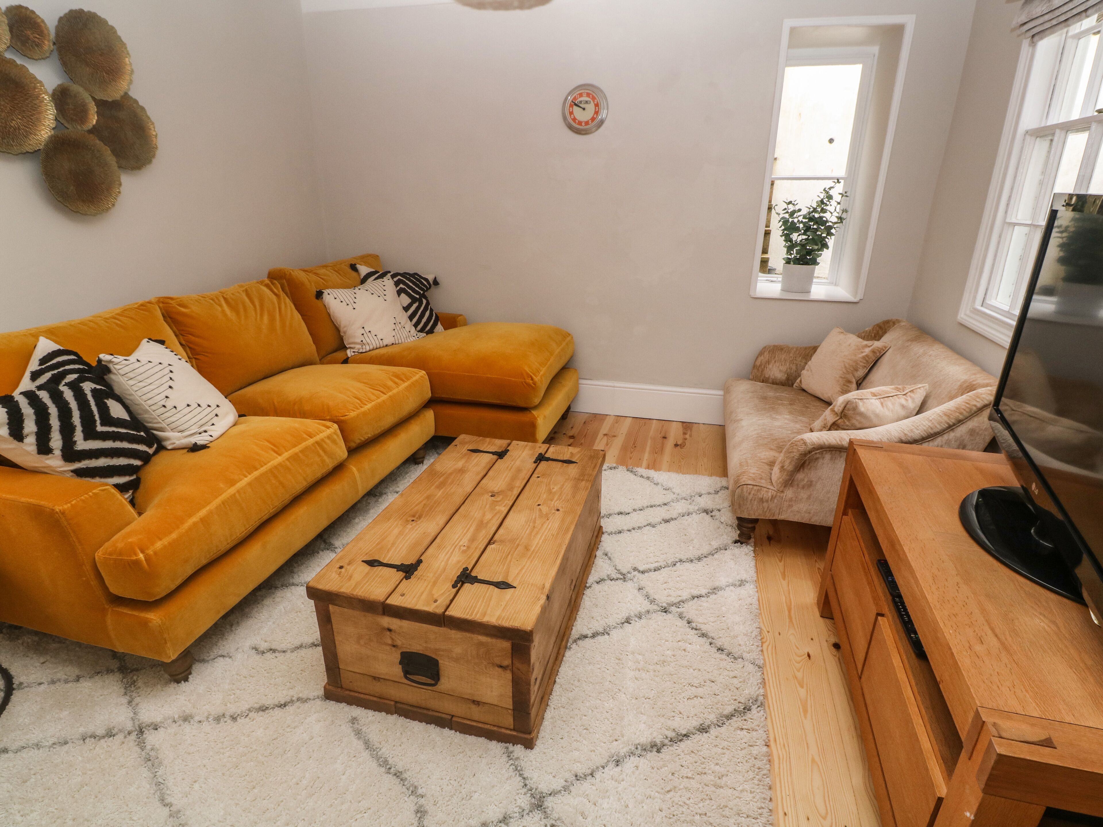 A living room with a mustard sofa, a beige armchair, a wooden coffee table, and a TV on a wooden stand.
