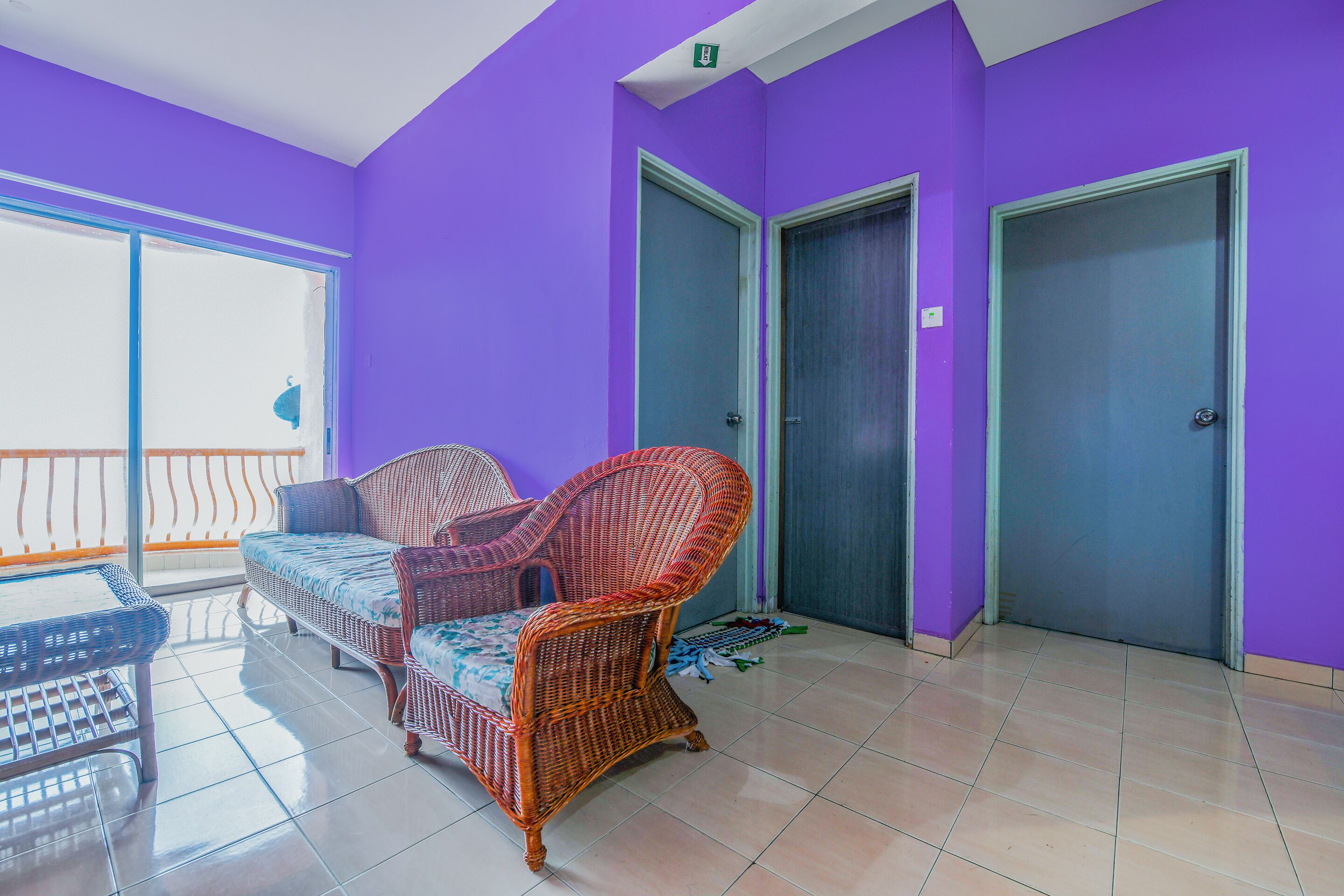 Quarto com paredes roxas, mobiliário de vime e chão de azulejos.