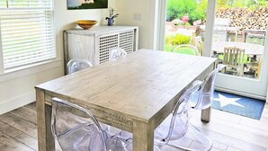 A dining area with a wooden table and chairs, a hanging light fixture, a painting on the wall, and a view of the outdoors through a glass door. - Beautiful 4 bed with Pool + Spa (Nantucket)