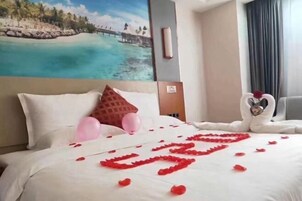 Una habitación de hotel con una cama, un cuadro de una escena de playa y una decoración con forma de corazón hecha de pétalos de rosa.