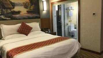 A hotel room with a bed, a shower, and a bathroom visible through a glass door.