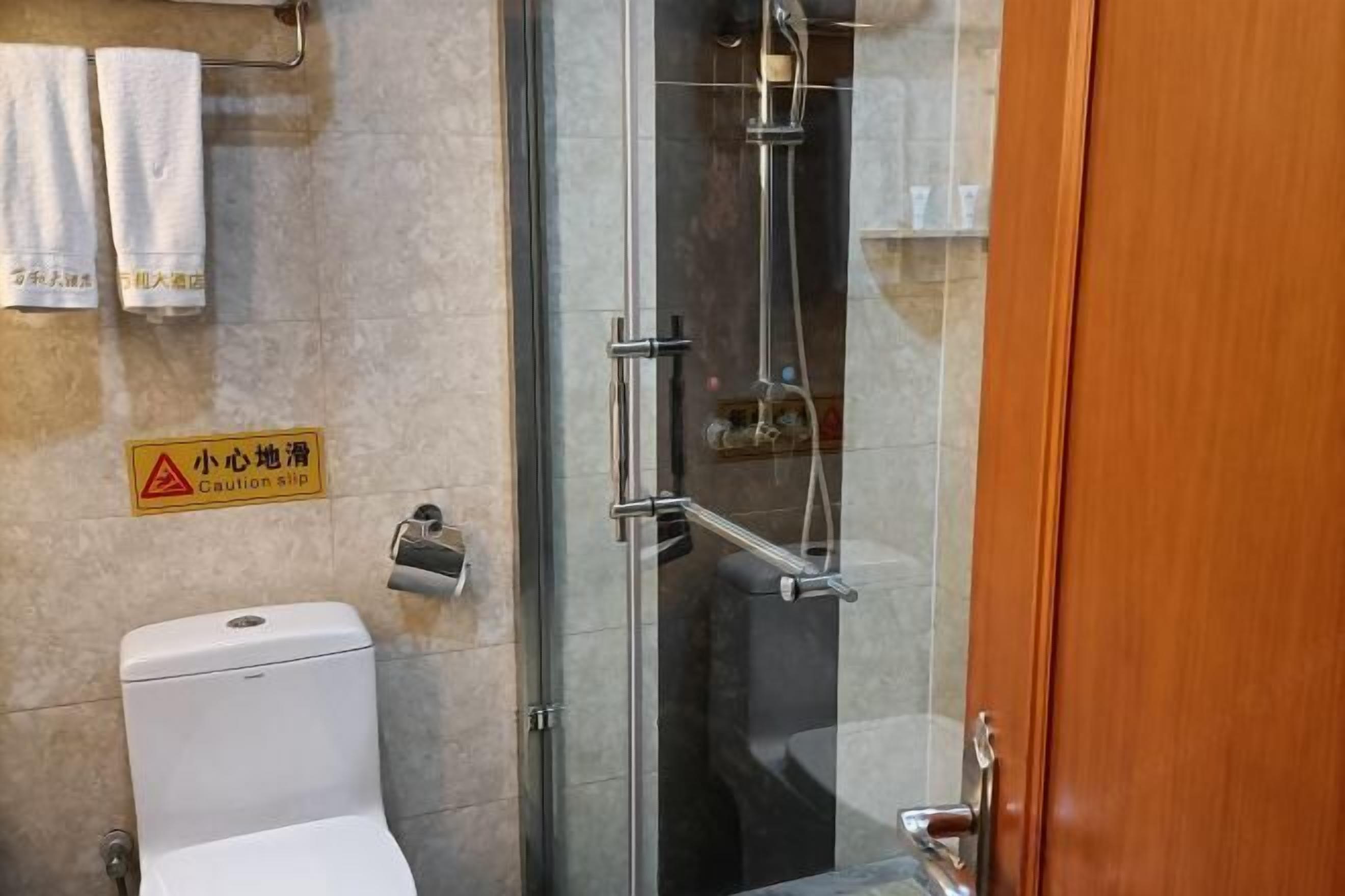 A bathroom with a glass shower enclosure, a toilet, and a caution sign on the wall.