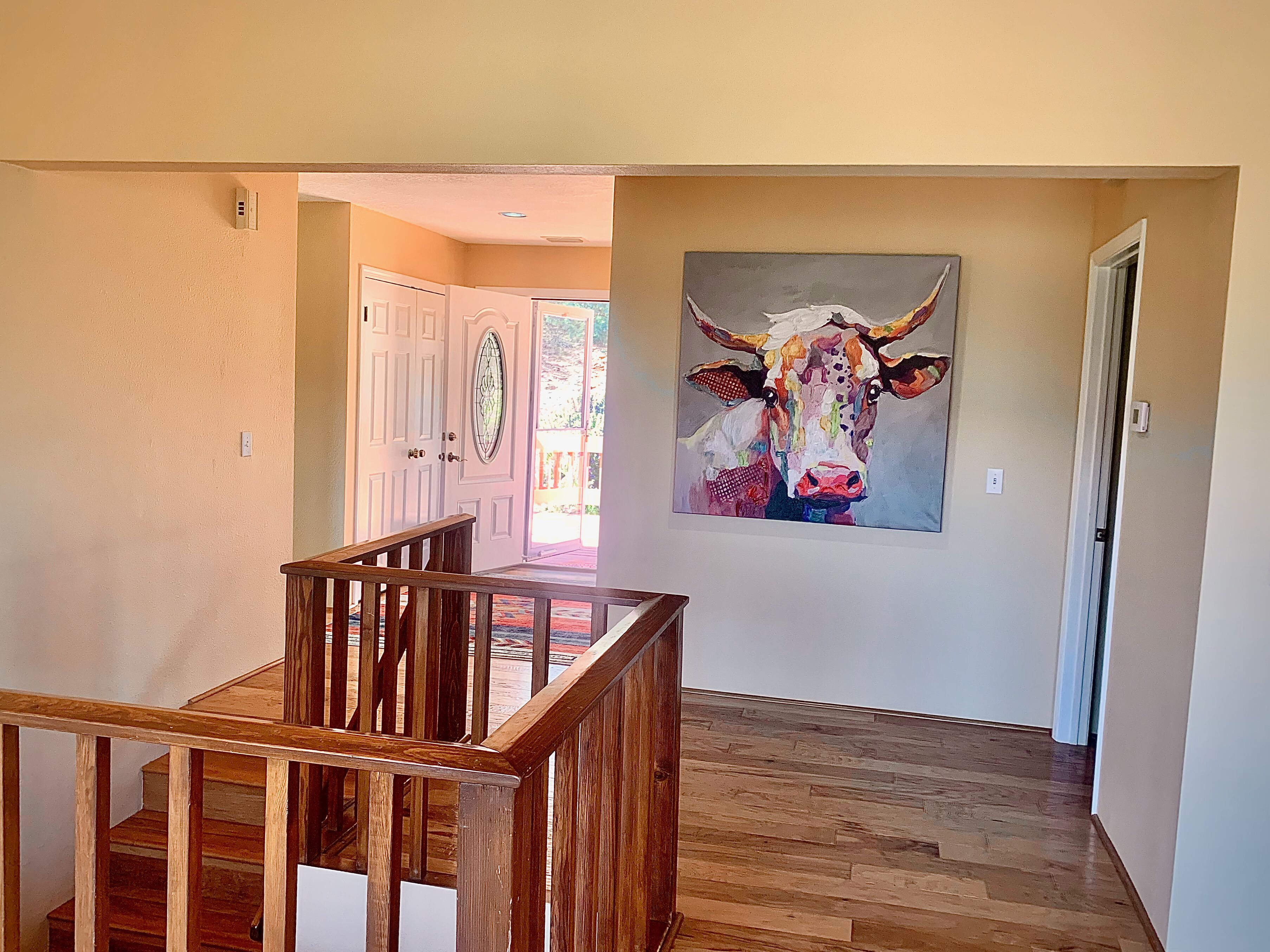 A hallway with wooden flooring, a staircase, and a painting of a cow on the wall.