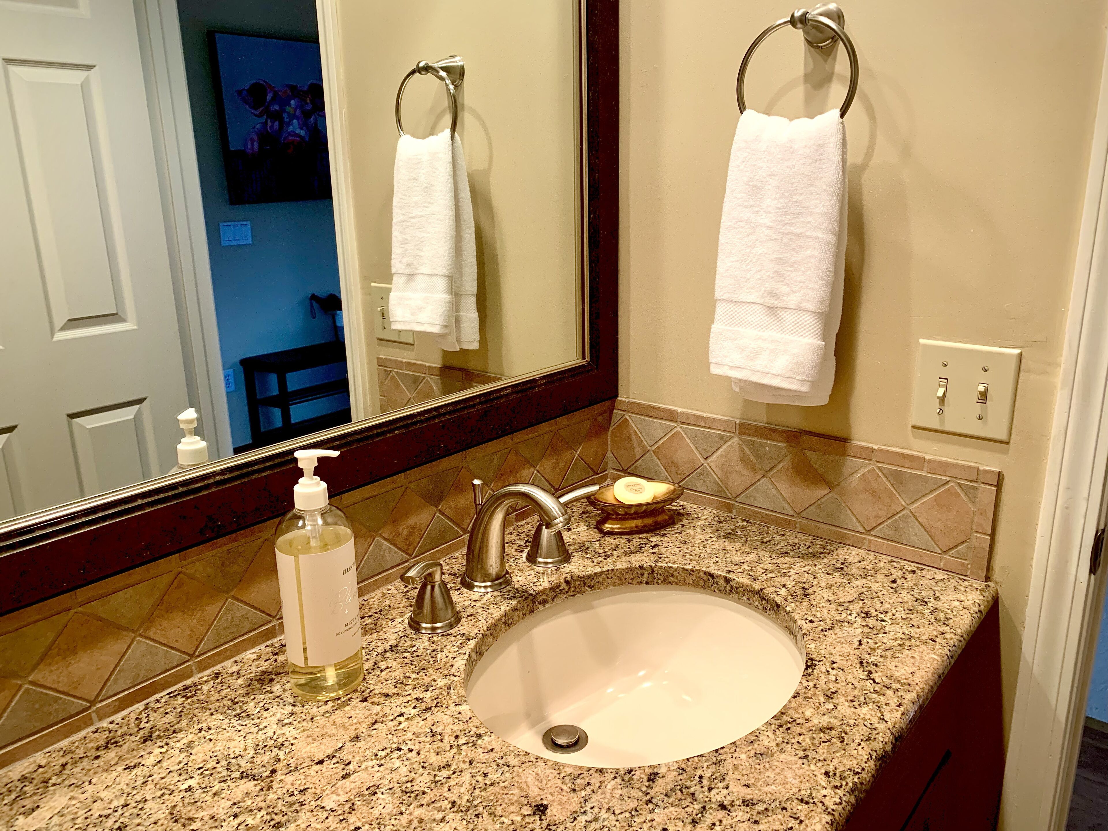 A bathroom with a granite countertop, a sink, a mirror, and two white towels hanging on towel rings.