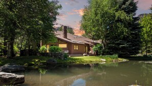 A rustic cabin with a stone foundation, surrounded by a pond and lush greenery. - Hermosa Haven | Red Cliff Views, Garage, 30+ Stay (Durango)