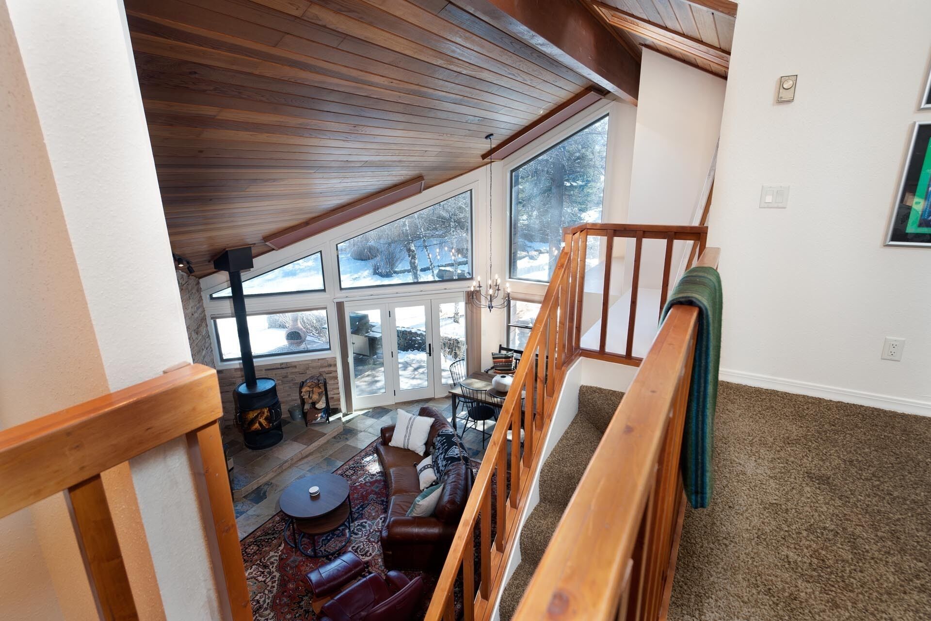 A cozy loft-style living area with a fireplace, a staircase, and large windows offering a view of the outdoors.