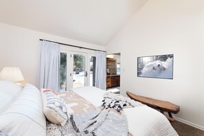 Ein Schlafzimmer mit Bett, einer Bank, einem Fernseher und einer Glastür zu einem Badezimmer.