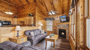 Een gezellig cabin-interieur met houten plafond, open haard, bank, televisie en een keukenhoek.