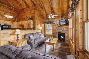 Ein gemütliches Blockhausschlafzimmer mit Holzbalkendecke, Kamin, einer Couch, einem Fernseher und einer Küchenzeile.