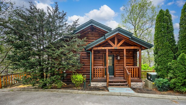 Een vakantiehuisje van hout met een veranda, omringd door bomen en een heldere lucht.