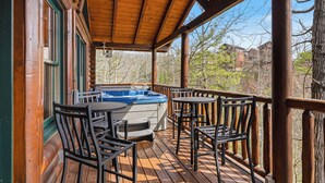 Een houten terras met een jacuzzi, buitenmeubels en uitzicht op bomen en huizen.