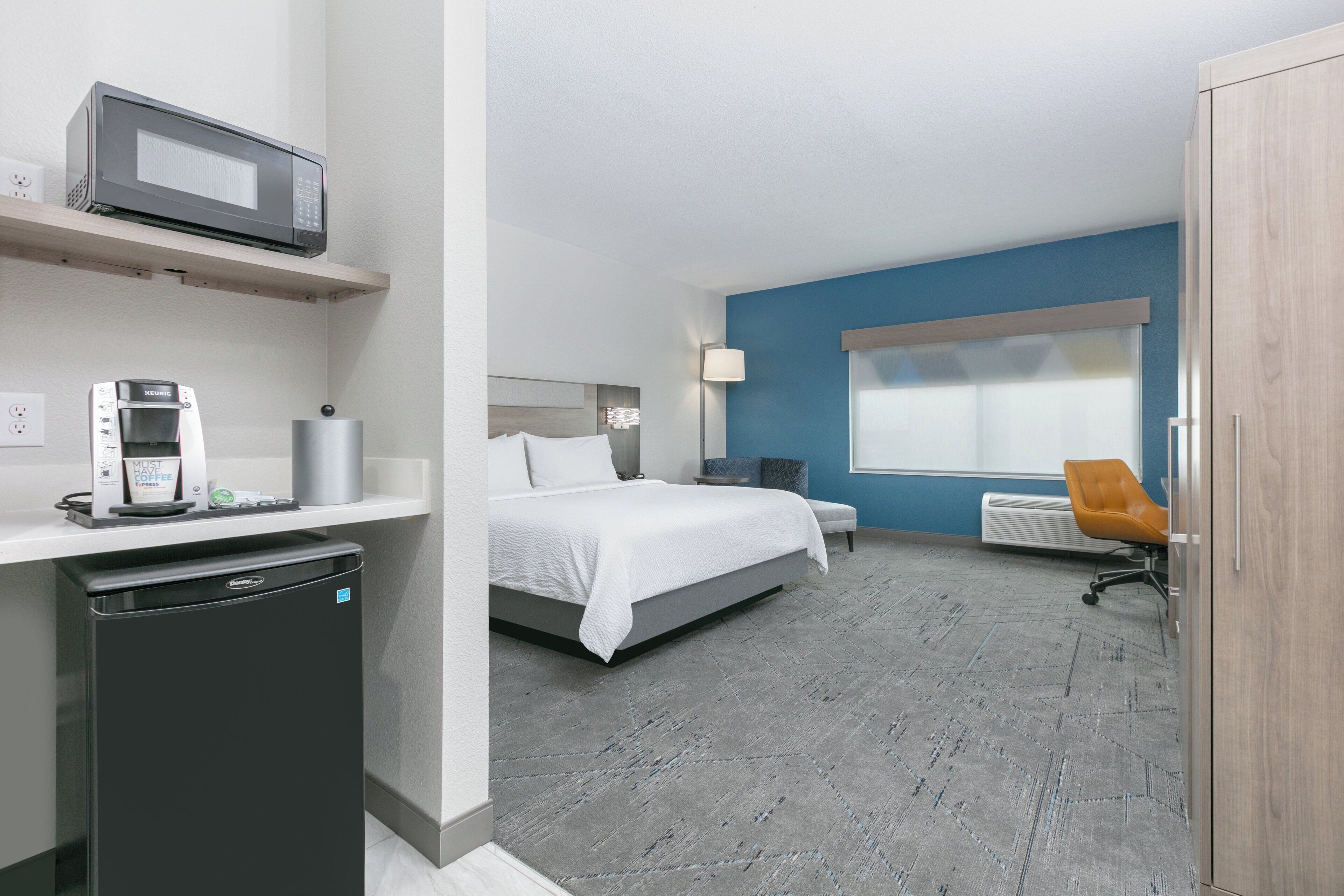 Une chambre d’hôtel équipée d’un lit, d’un bureau, d’un four à micro-ondes, d’une machine à café et d’un petit réfrigérateur.