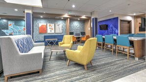 Un espace de détente moderne, doté de sièges confortables, d’un téléviseur et d’une fresque murale représentant un paysage urbain.