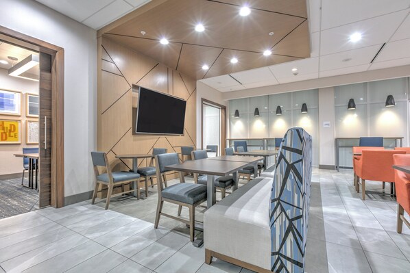 A modern conference room with a large screen, multiple tables, and chairs.