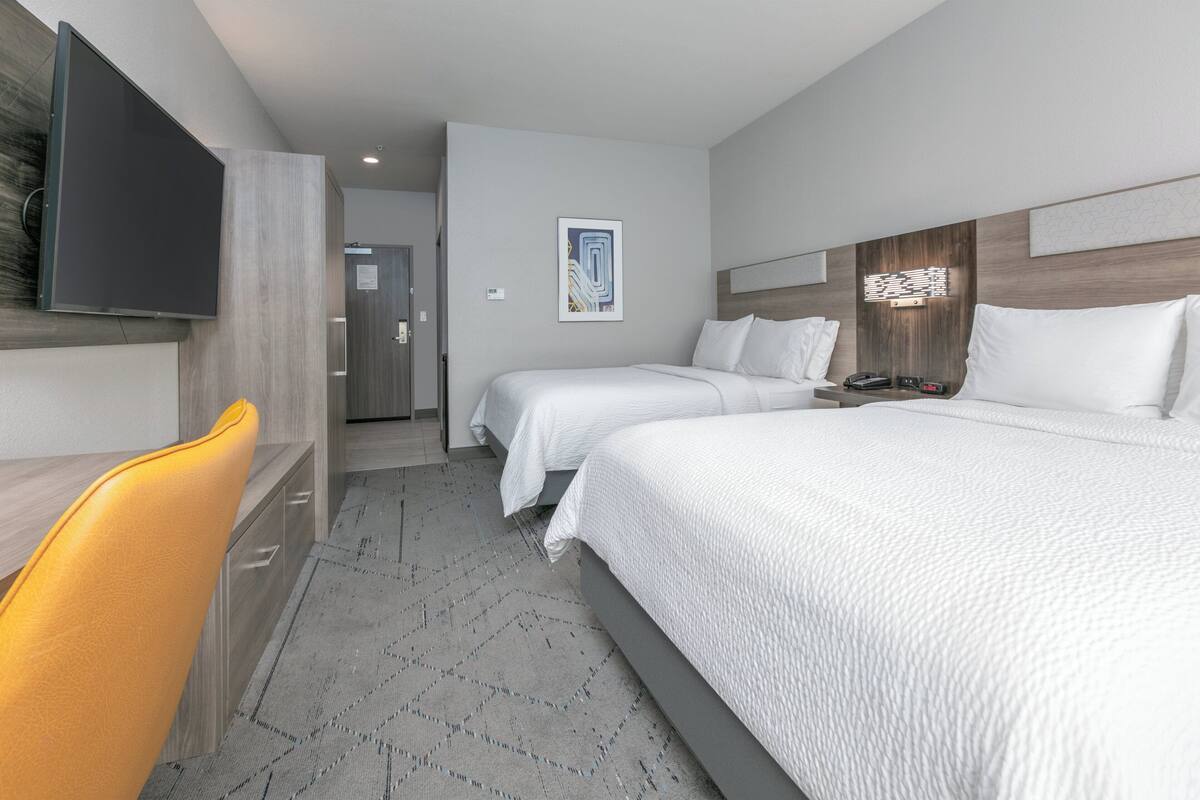 A hotel room with two beds, a desk, a chair, and a television.