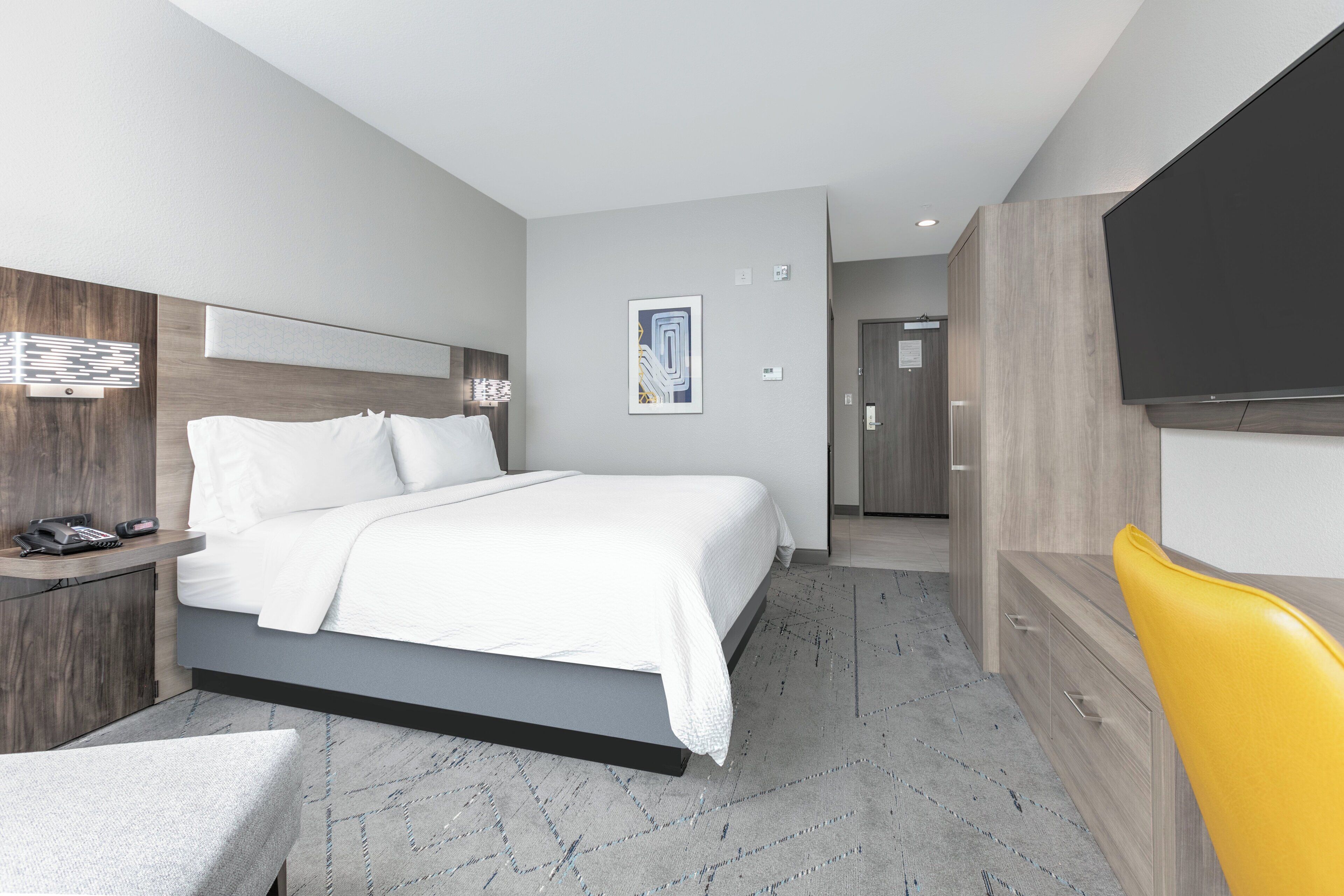 Una habitación de hotel moderna con cama, mesita de noche y televisor.