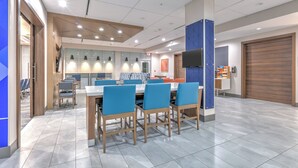 Un espace repas moderne avec une longue table et des chaises bleues, un coin cuisine équipé d’un four à micro-ondes et une grande porte en bois.
