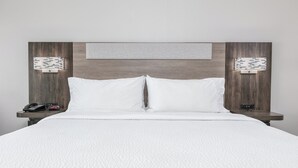 Une chambre d’hôtel avec un grand lit, deux tables de chevet, un luminaire fixé au mur et une petite horloge.