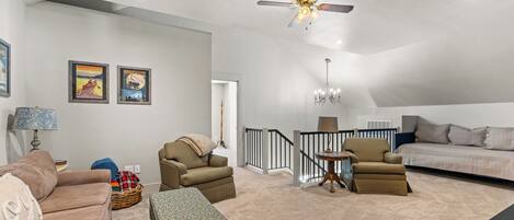 A spacious living room with a high ceiling, a ceiling fan, a chandelier, and a staircase leading to an upper level.