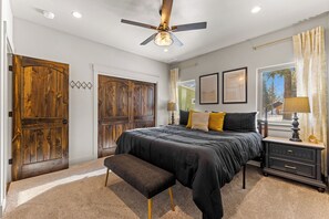 A bedroom with a large bed, a ceiling fan, wooden doors, a bench, a nightstand, and a window with curtains. - Fun Amok - Warren Wagon Rd - WiFi - Large driveway - Hot tub (McCall)