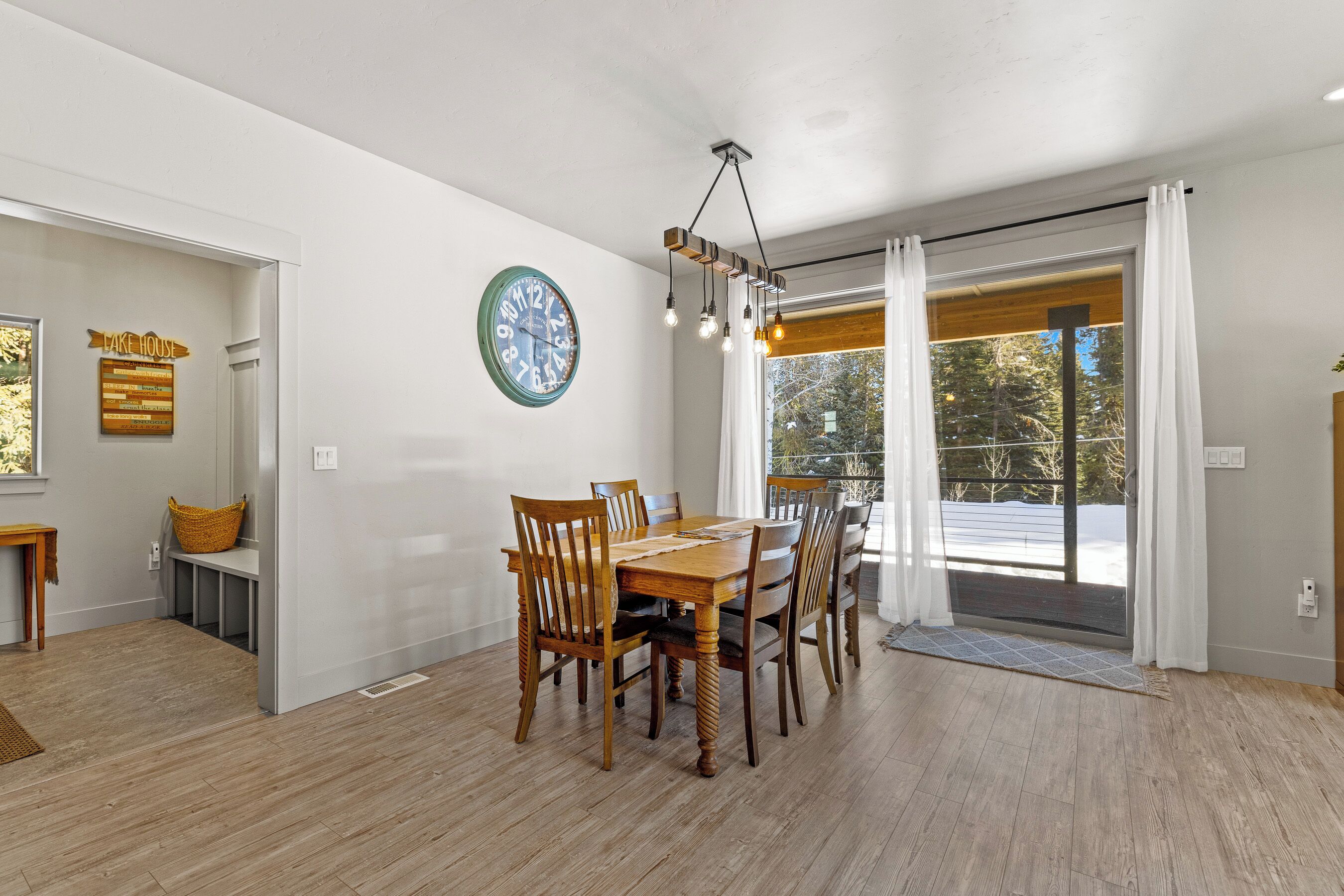Un coin repas avec une table et des chaises en bois, une horloge murale et une vue à travers une porte vitrée.