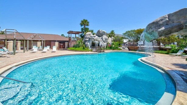 A clear blue pool with a rock feature and lounge chairs.