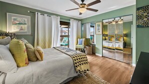 A bedroom with a bed, a ceiling fan, a wardrobe with mirrors, and a view of the outside.