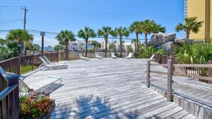 A wooden deck with lounge chairs, palm trees, and a large rock.