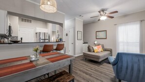 Un salon moderne comprenant un coin repas, un ventilateur de plafond et une grande fenêtre équipée de stores.