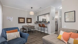 Un salon moderne avec un canapé bleu, un canapé gris et un coin repas comprenant une table et des chaises.