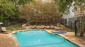 Une piscine rectangulaire bordée de pierres, entourée d’une clôture et d’arbres.