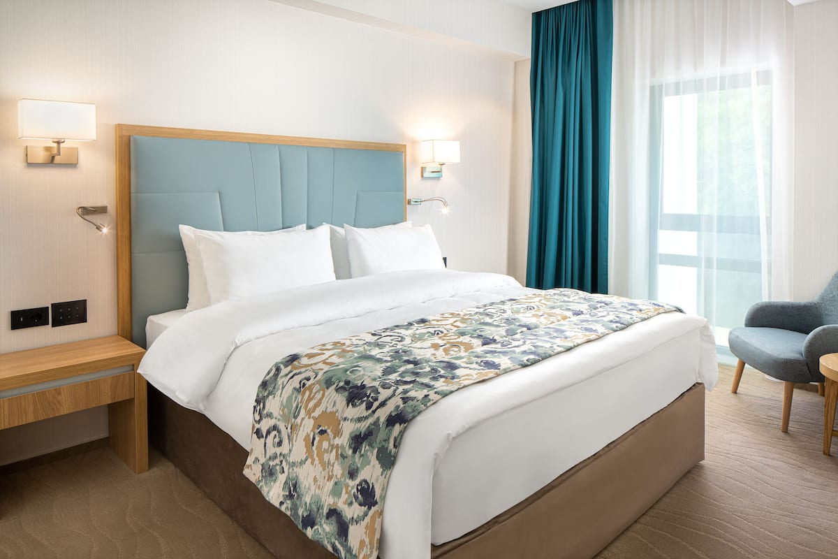 A hotel room with a large bed, a nightstand, a desk, a chair, and a window with curtains.