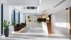 Eine moderne Hotelhalle mit einer Rezeption, einer Sitzecke und großen Fenstern, die für natürliches Licht sorgen.