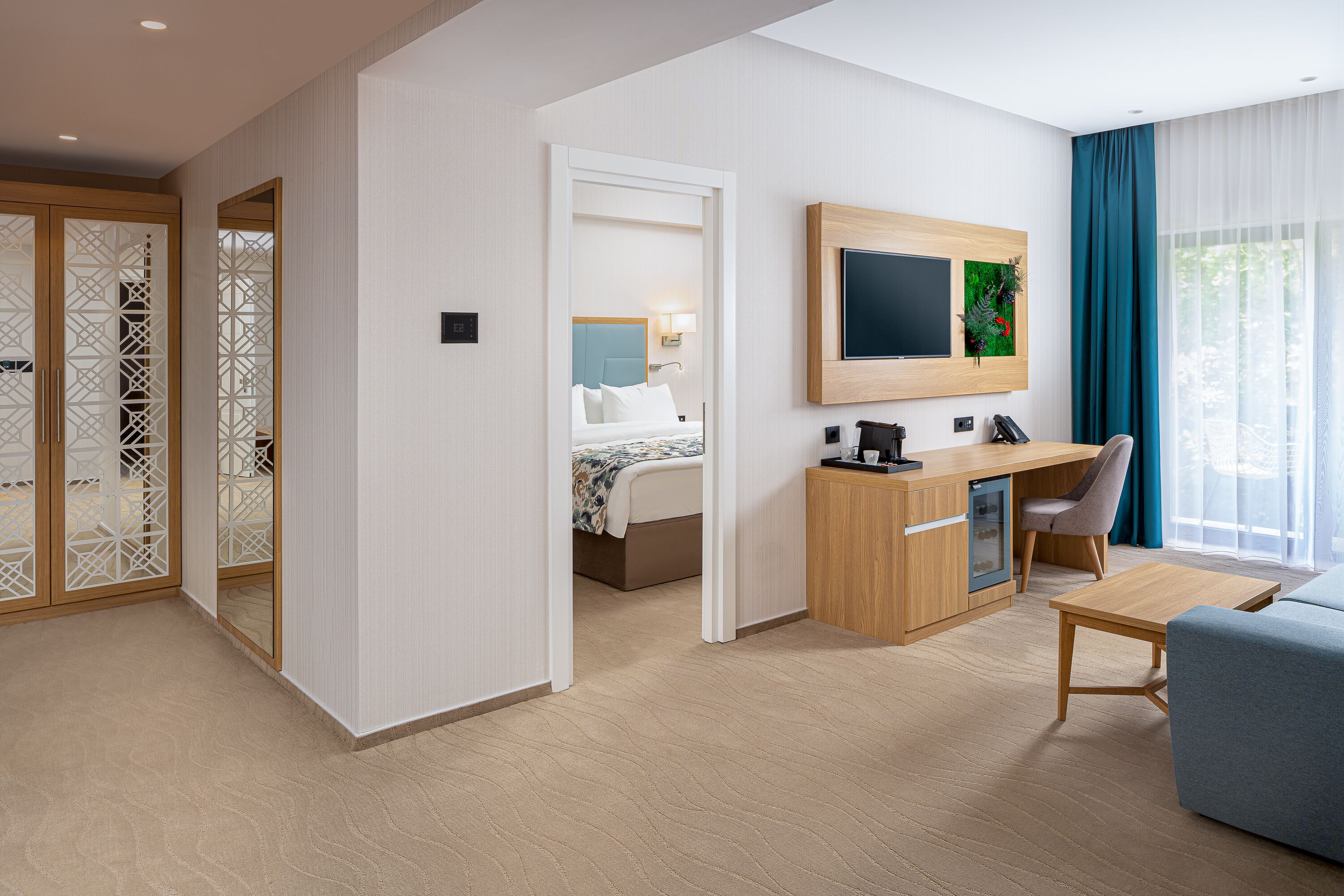 A modern hotel room with a bed, desk, chair, TV, and a view of the outdoors.
