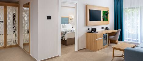 A modern hotel room with a bed, desk, chair, TV, and a view of the outdoors.