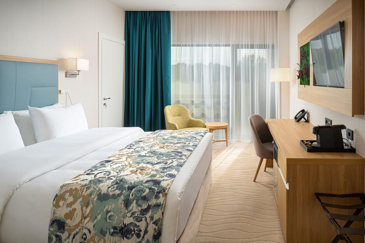 A hotel room with a large bed, a desk with a chair, a small table, and a TV mounted on the wall.