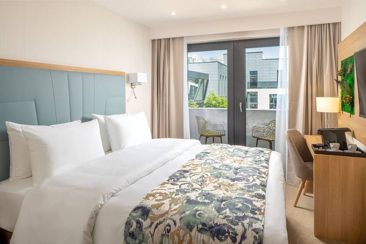 A hotel room with a large bed, a desk, a chair, and a view of the outside.